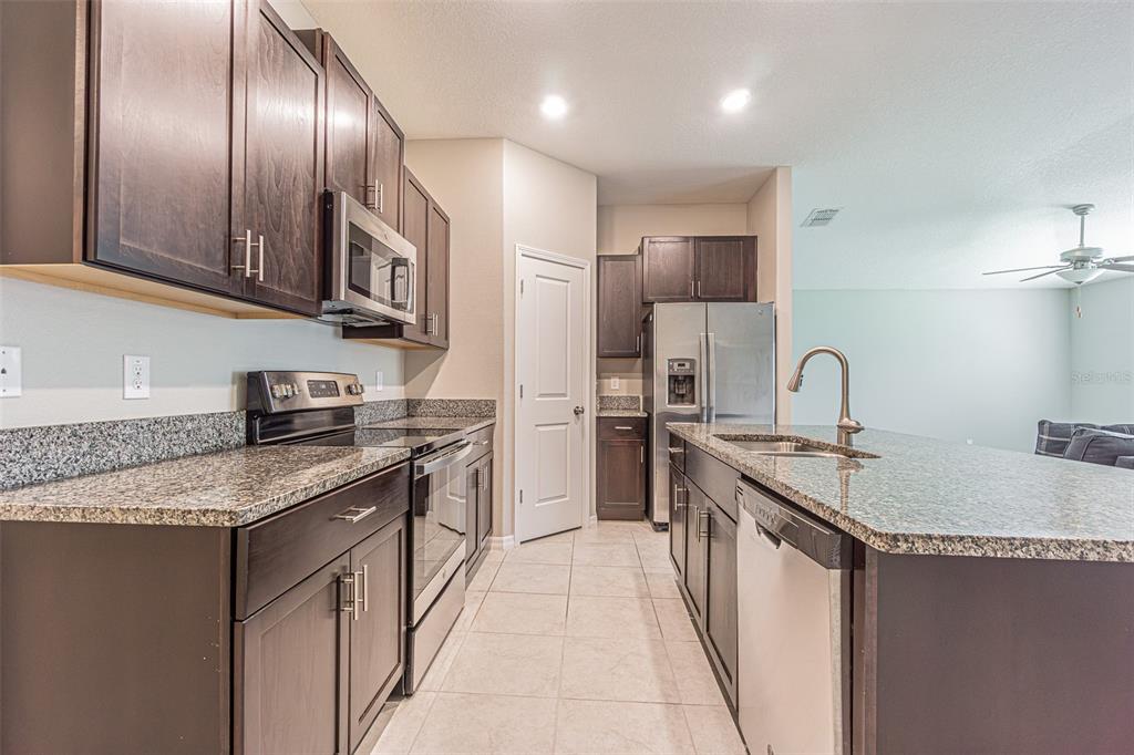 A kitchen with dark wood cabinets, granite countertops, stainless steel appliances, and a center island — 13009 MAJESTIC GARDEN LANE, RIVERVIEW, FL