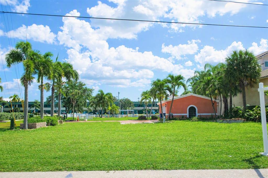 A grassy backyard features palm trees, a detached orange garage, and a white picket fence — 11855 1ST STREET E, TREASURE ISLAND, FL