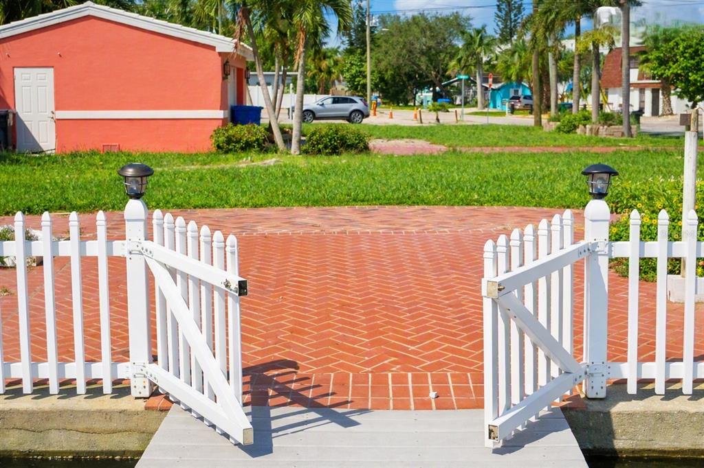 A white picket fence with an open gate leads to a red brick patio area — 11855 1ST STREET E, TREASURE ISLAND, FL