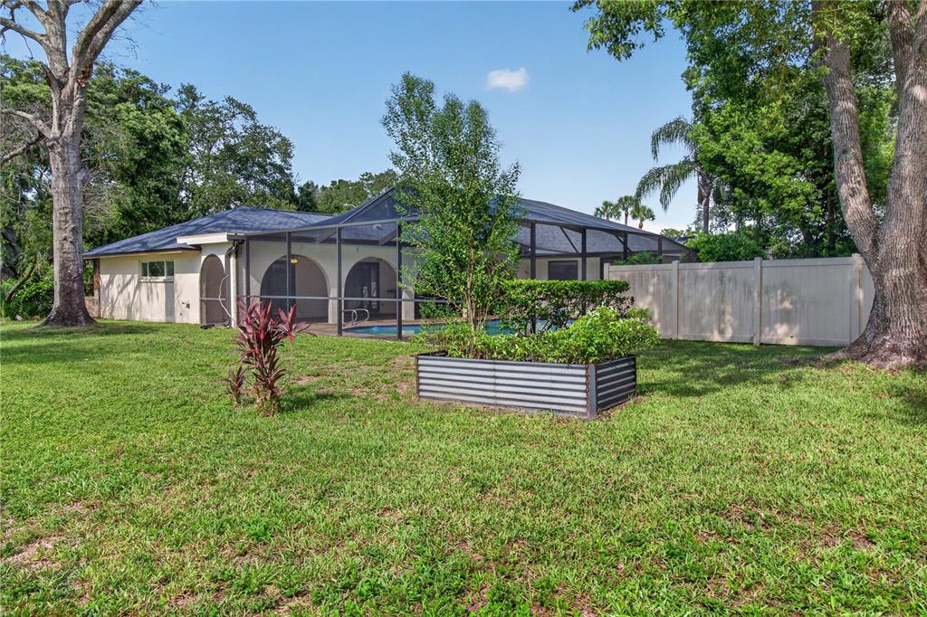 A backyard view of a house with a screened-in pool, raised garden bed, and fence — 10 LINDEN LANE, PALM HARBOR, FL