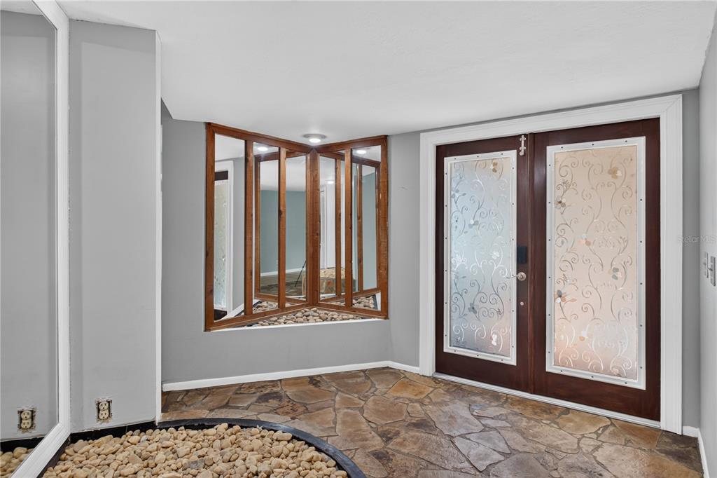 An entryway features a stone floor, a rock-filled planter, mirrored walls, and double glass doors — 10 LINDEN LANE, PALM HARBOR, FL