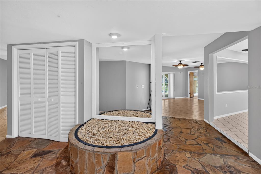 A room with a stone-tiled floor, a circular stone planter, and a large wall mirror — 10 LINDEN LANE, PALM HARBOR, FL