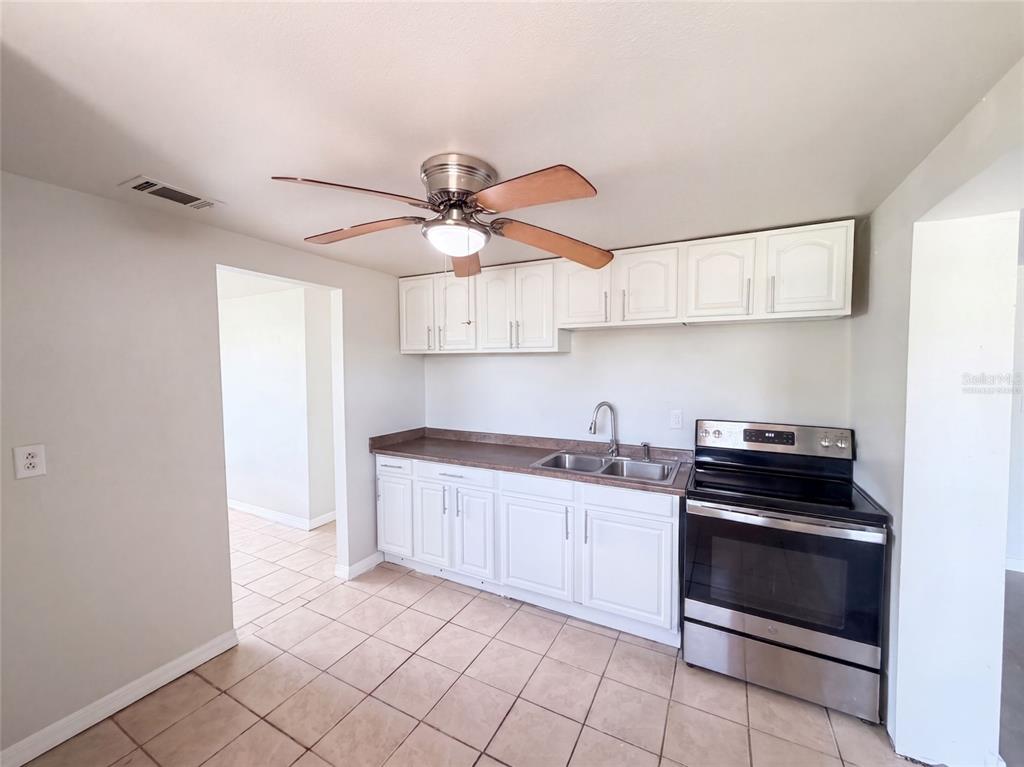 A kitchen features white cabinets, a stainless steel stove, a double sink, and tiled flooring — 2213 BOUYER STREET, LAKE WALES, FL
