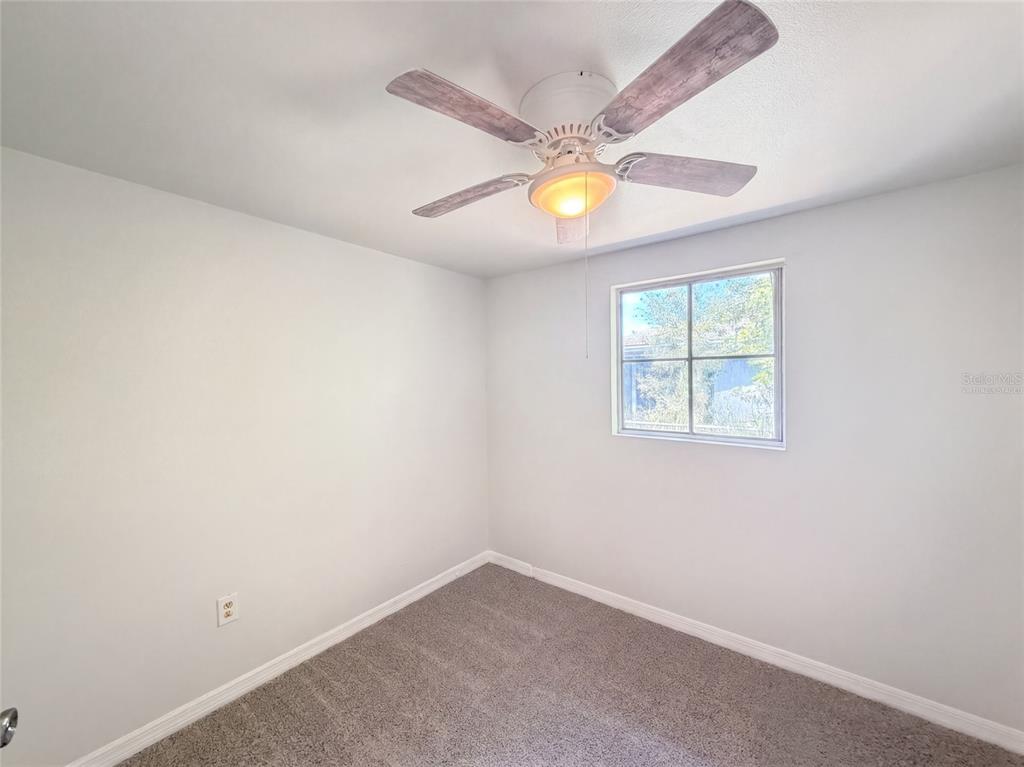 An empty bedroom features light gray walls, gray carpeting, a ceiling fan, and one window — 2213 BOUYER STREET, LAKE WALES, FL