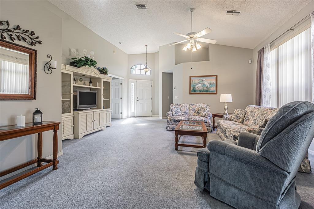 A living room features gray carpeting, floral sofas, a recliner, and an entertainment center — 13837 LEROUX DRIVE, HUDSON, FL