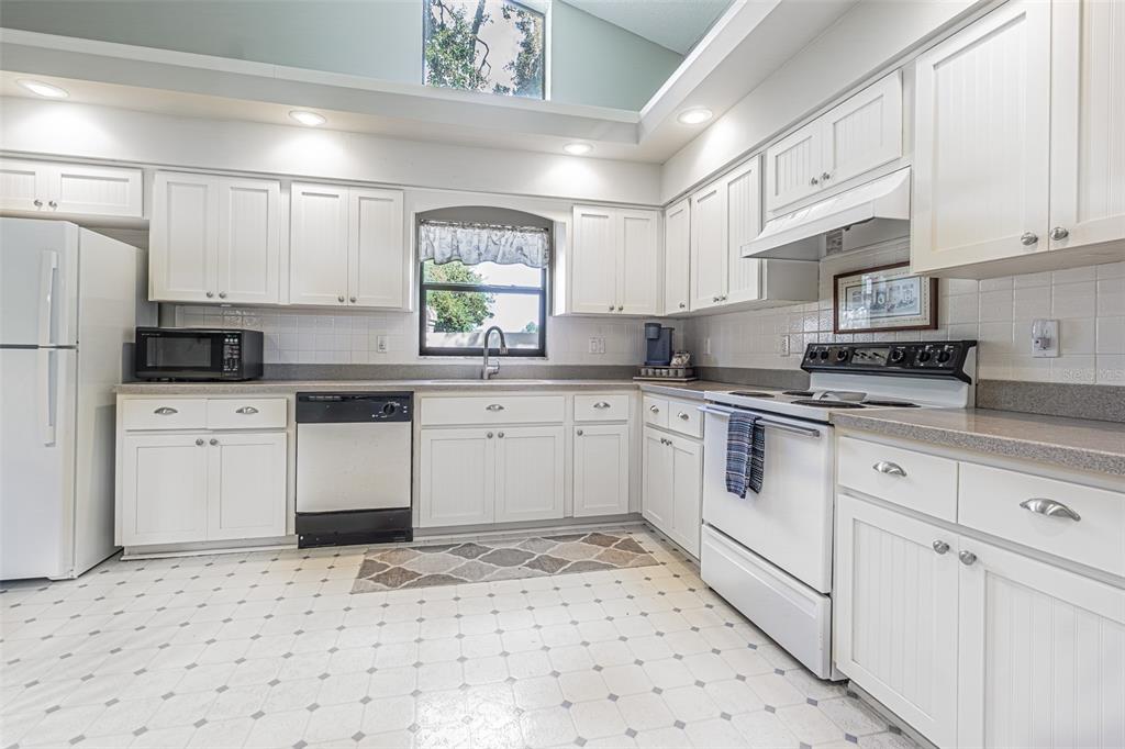 A kitchen features white cabinets, white appliances, a tiled floor, and a vaulted ceiling window — 13837 LEROUX DRIVE, HUDSON, FL