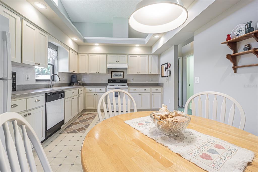 A kitchen with white cabinets, light countertops, and a dining table in the foreground — 13837 LEROUX DRIVE, HUDSON, FL