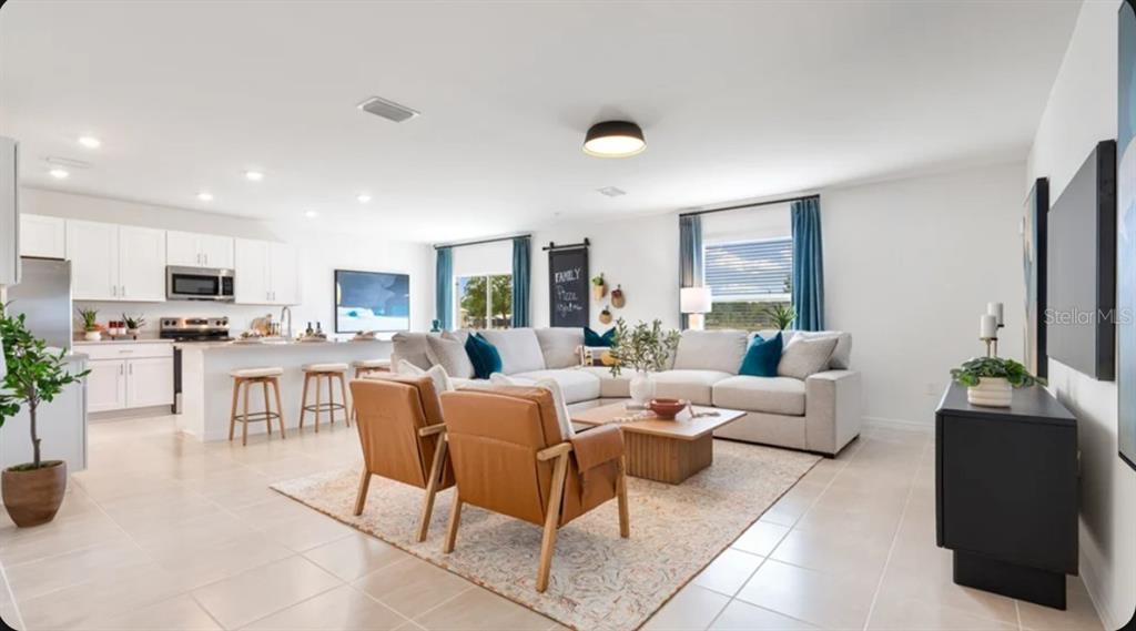 An open-concept living room and kitchen with white cabinets, a sectional sofa, and leather chairs — 5327 LOGGIA LANE, KISSIMMEE, FL
