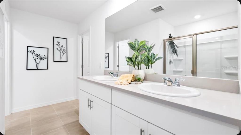 A bright bathroom features a double vanity with white cabinets, quartz countertops, and a mirror — 5327 LOGGIA LANE, KISSIMMEE, FL