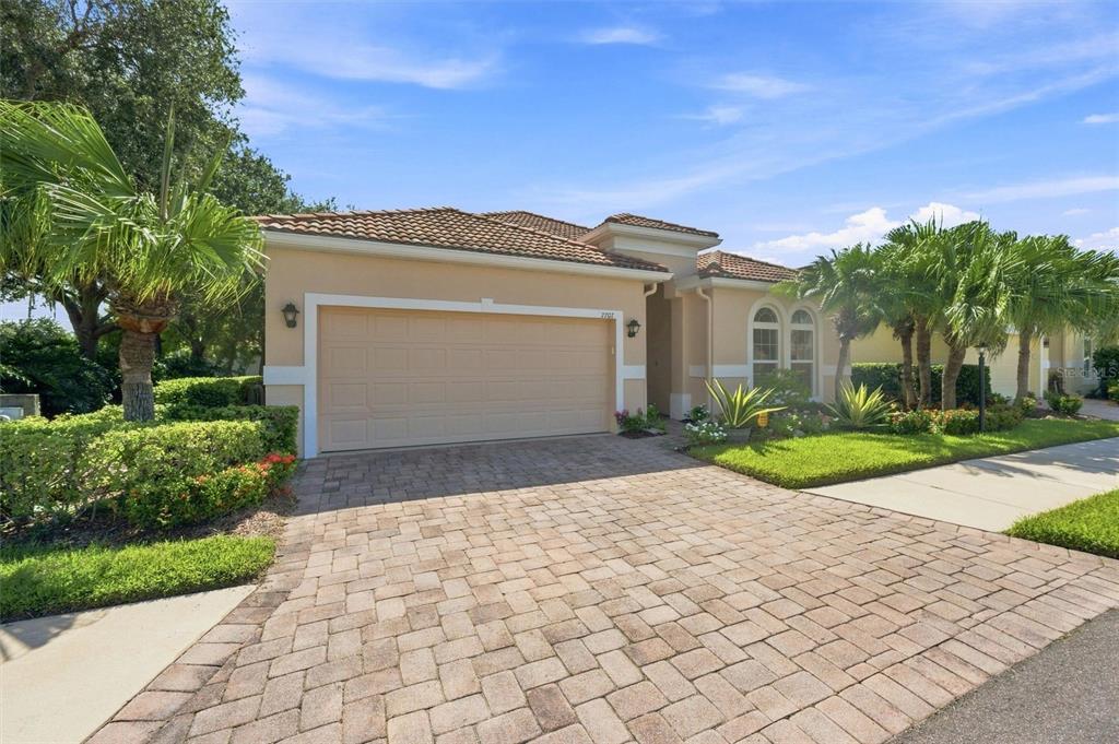 A single-story house with a beige stucco exterior, a tiled roof, and a paved driveway — 7707 33RD STREET E, SARASOTA, FL