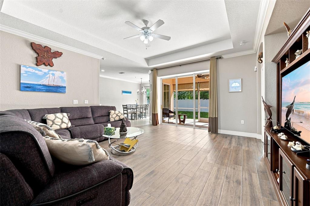 A living room features a dark sectional sofa, wood-look tile floors, and a sliding glass door — 7707 33RD STREET E, SARASOTA, FL
