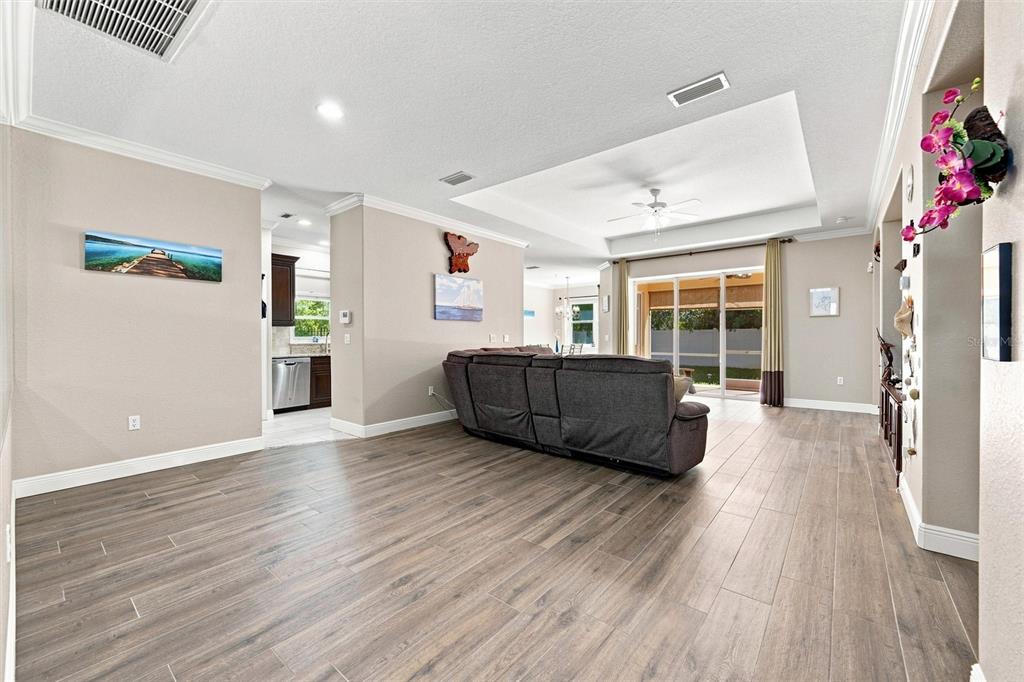 An open-concept living room features wood-look tile flooring, a tray ceiling, and a gray sofa — 7707 33RD STREET E, SARASOTA, FL