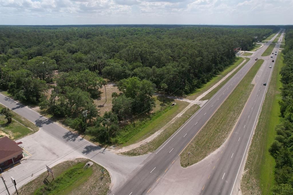 An aerial view shows a wooded lot situated between a highway and a side road — 24926 E COLONIAL DRIVE, CHRISTMAS, FL