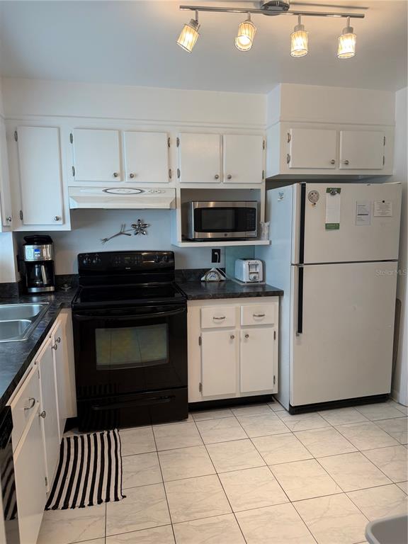 A kitchen features white cabinets, a black stove, a white refrigerator, and tiled flooring — 1270 GULF BOULEVARD UNIT 707, CLEARWATER BEACH, FL