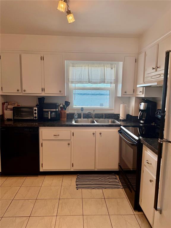 A kitchen with white cabinets, black appliances, tile flooring, and a window overlooking the water — 1270 GULF BOULEVARD UNIT 707, CLEARWATER BEACH, FL