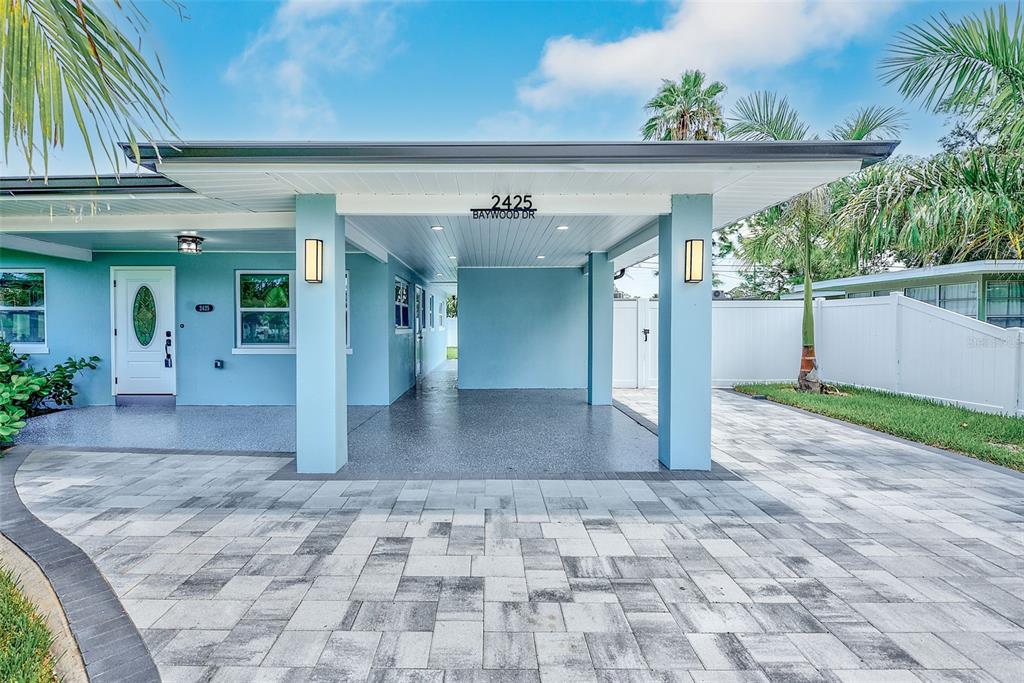 A light blue house exterior features a covered carport with a paved driveway and walkway — 2425 BAYWOOD DRIVE E, DUNEDIN, FL