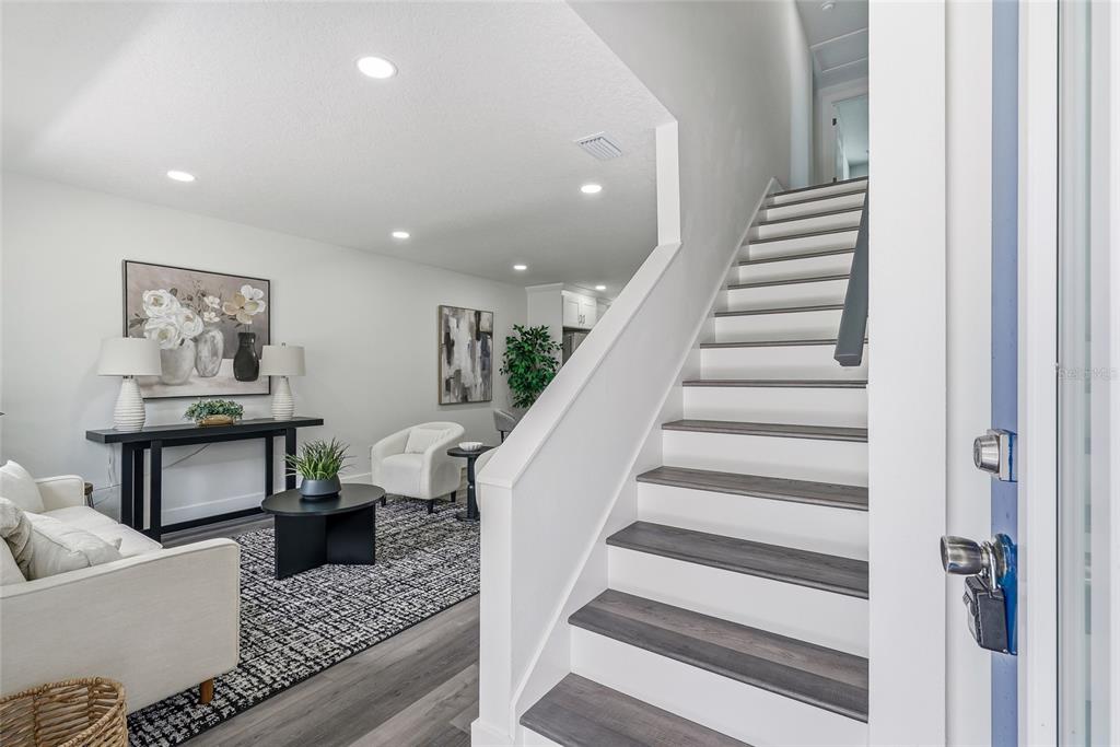 A living room with a staircase, white walls, and dark wood-look flooring — 15924 WINDING DR, TAMPA, FL