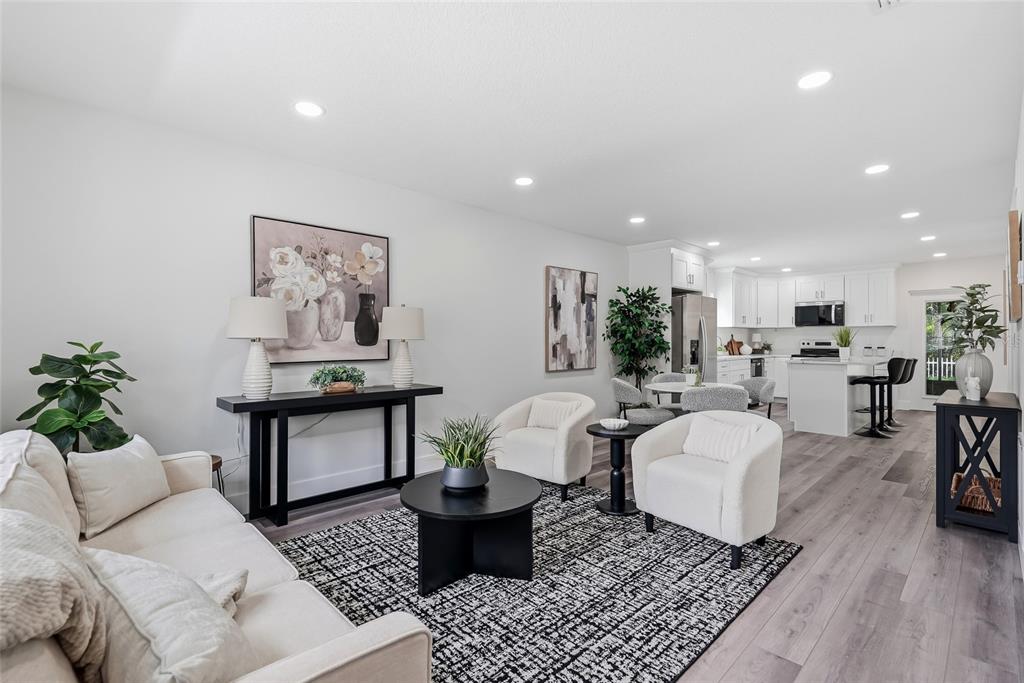 An open-concept living room and kitchen feature white cabinetry, light wood flooring, and modern furniture — 15924 WINDING DR, TAMPA, FL