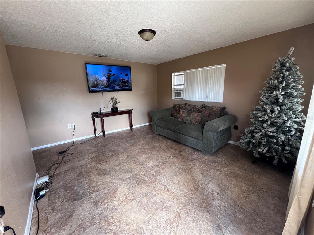 A living room features tan walls, tile flooring, a wall-mounted television, and a Christmas tree — 589 DUNCAN CIRCLE E, AUBURNDALE, FL