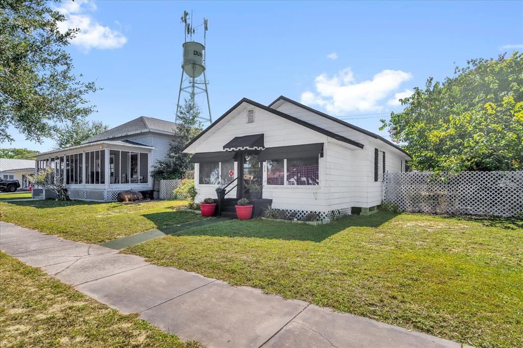 A white single-story house with black awnings stands next to a tall water tower — 312 E MAIN STREET, DUNDEE, FL