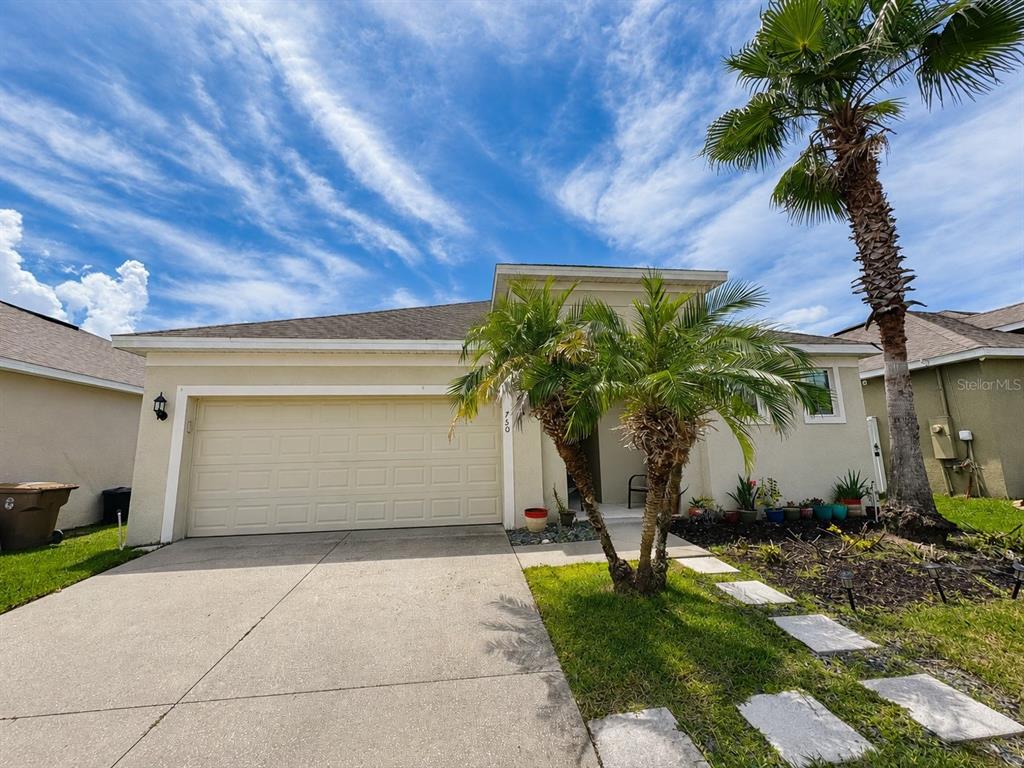 A single-story house with a beige stucco exterior, a two-car garage, and a palm tree — 750 STAR MAGNOLIA DRIVE, KISSIMMEE, FL