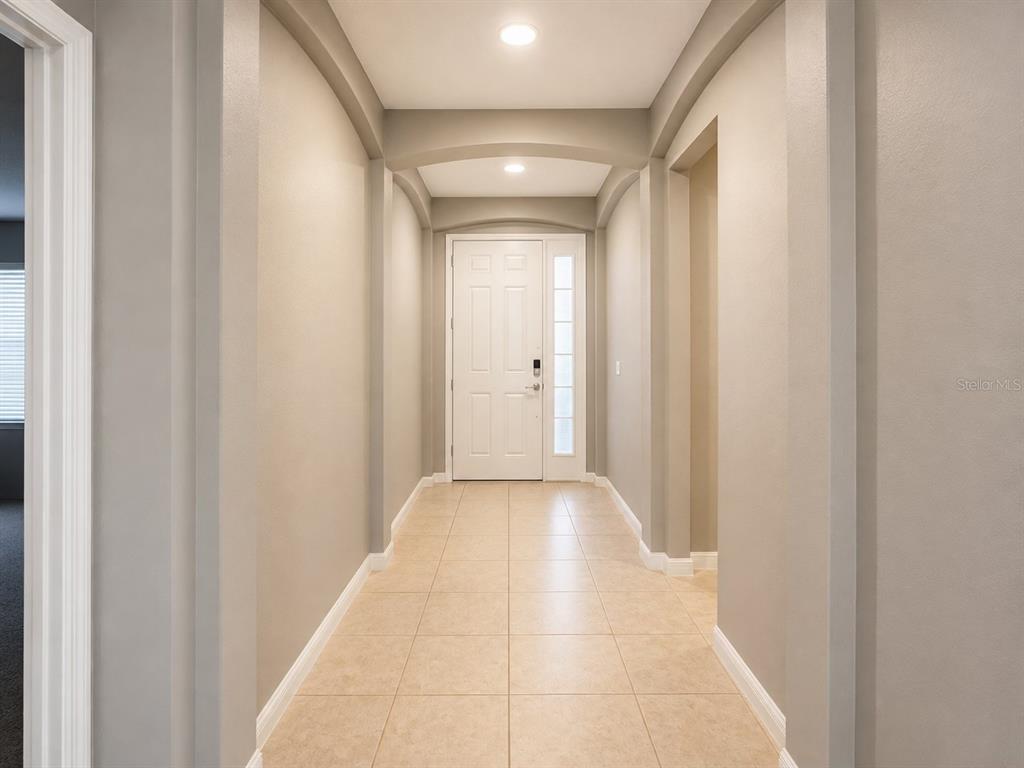 A hallway with beige tile flooring leads to a white front door with a sidelight — 750 STAR MAGNOLIA DRIVE, KISSIMMEE, FL