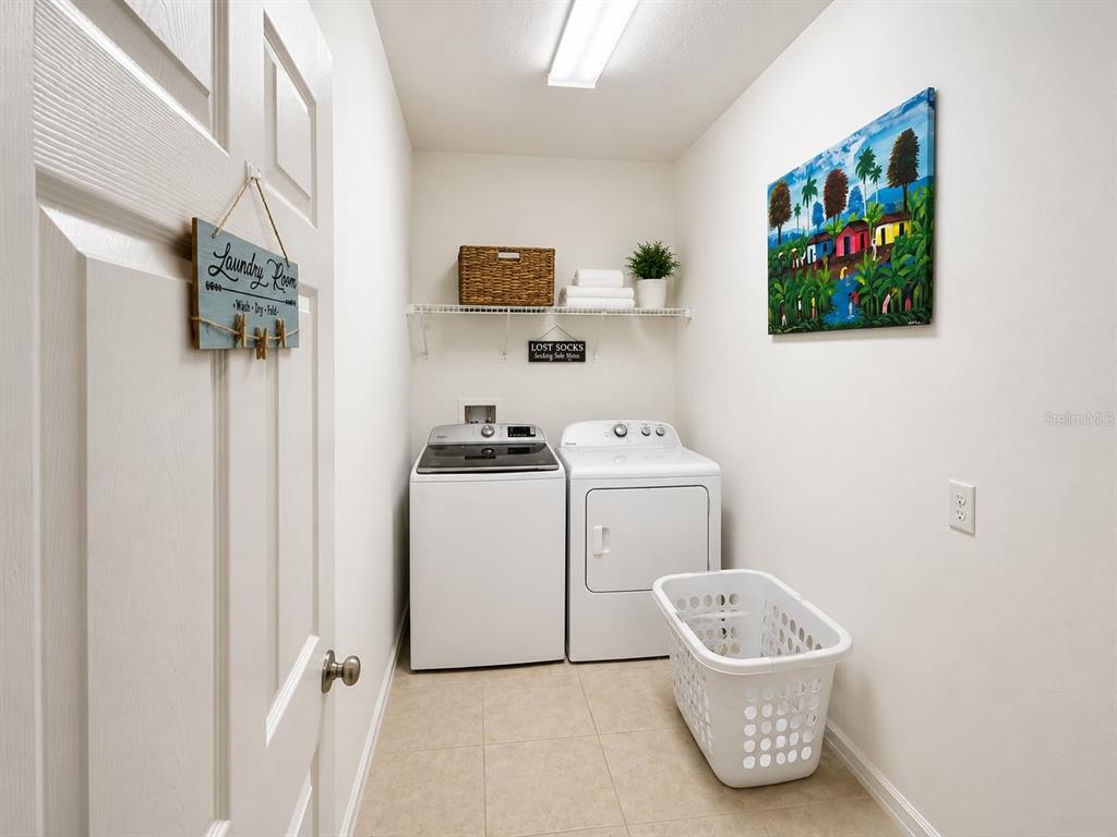 A laundry room with a washer, dryer, white tile flooring, and a wall-mounted storage shelf — 750 STAR MAGNOLIA DRIVE, KISSIMMEE, FL