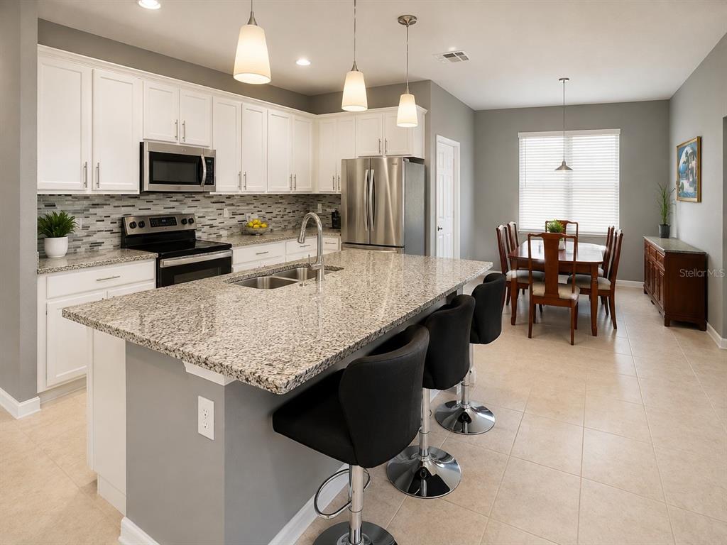 A kitchen with white cabinets, granite countertops, a center island, and an adjacent dining area — 750 STAR MAGNOLIA DRIVE, KISSIMMEE, FL
