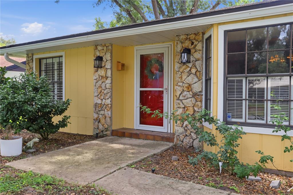 A yellow house exterior features a stone-accented entryway with a red front door — 1701 WIND WILLOW ROAD, BELLE ISLE, FL