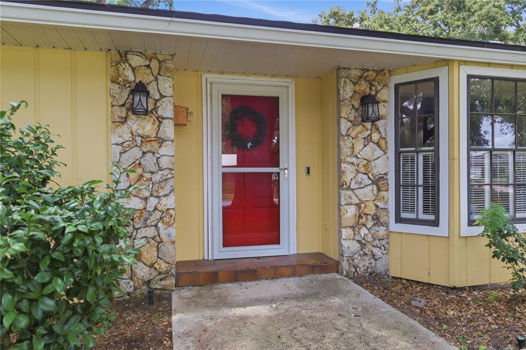 A yellow house exterior features a red front door, stone accents, and a concrete porch — 1701 WIND WILLOW ROAD, BELLE ISLE, FL