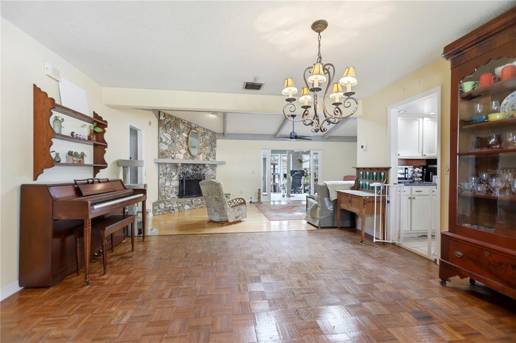A living room with parquet flooring, a piano, a stone fireplace, and a dining hutch — 1701 WIND WILLOW ROAD, BELLE ISLE, FL