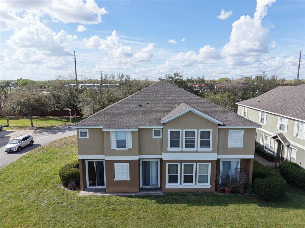 The rear exterior of a two-story tan house features multiple windows, sliding glass doors, and a shingled roof — 2018 ESTANCIA CIRCLE UNIT C, KISSIMMEE, FL