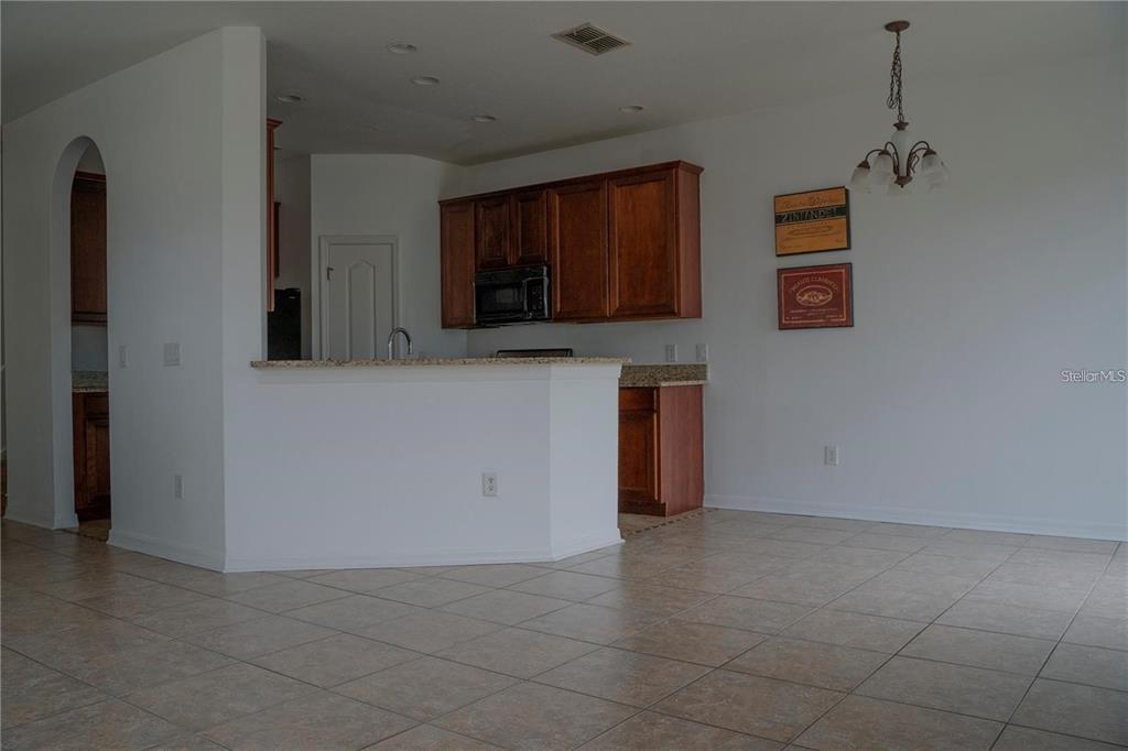 A kitchen with wood cabinets, granite countertops, and tile flooring opens to a dining area — 2018 ESTANCIA CIRCLE UNIT C, KISSIMMEE, FL