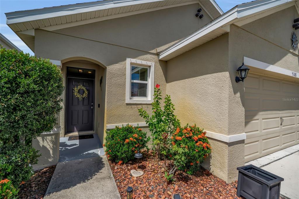 The exterior of a beige house features a dark front door, a garage, and landscaping — 5108 OLD TURNER LANE, PALMETTO, FL