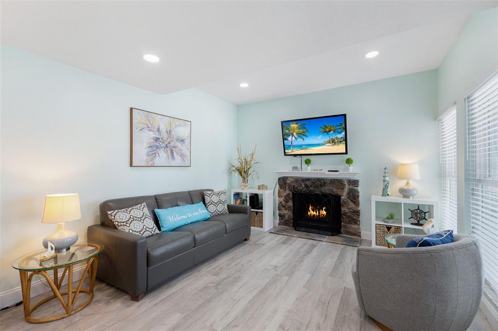 A living room features a grey sofa, stone fireplace with a mounted television, and light flooring — 337 REX PLACE UNIT G, MADEIRA BEACH, FL