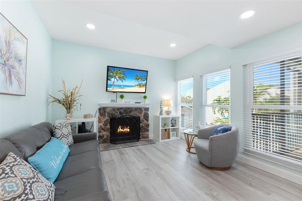 A living room features a stone fireplace, a wall-mounted television, and light-colored wood flooring — 337 REX PLACE UNIT G, MADEIRA BEACH, FL