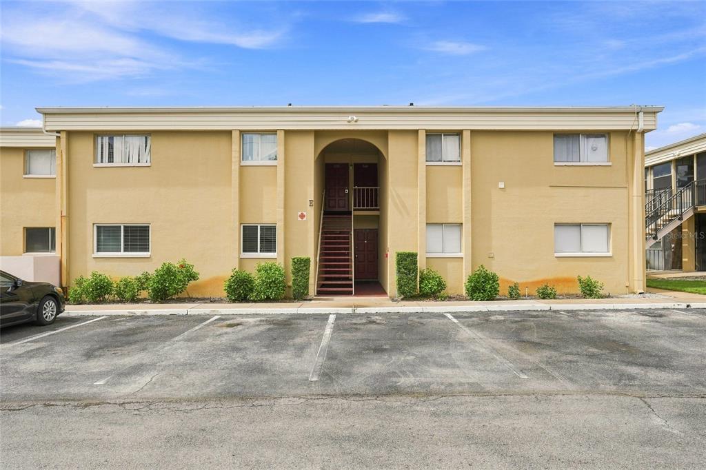 A two-story tan apartment building with an arched entryway and a parking lot in front — 1000 LAKE OF THE WOODS BOULEVARD UNIT 105E, FERN PARK, FL