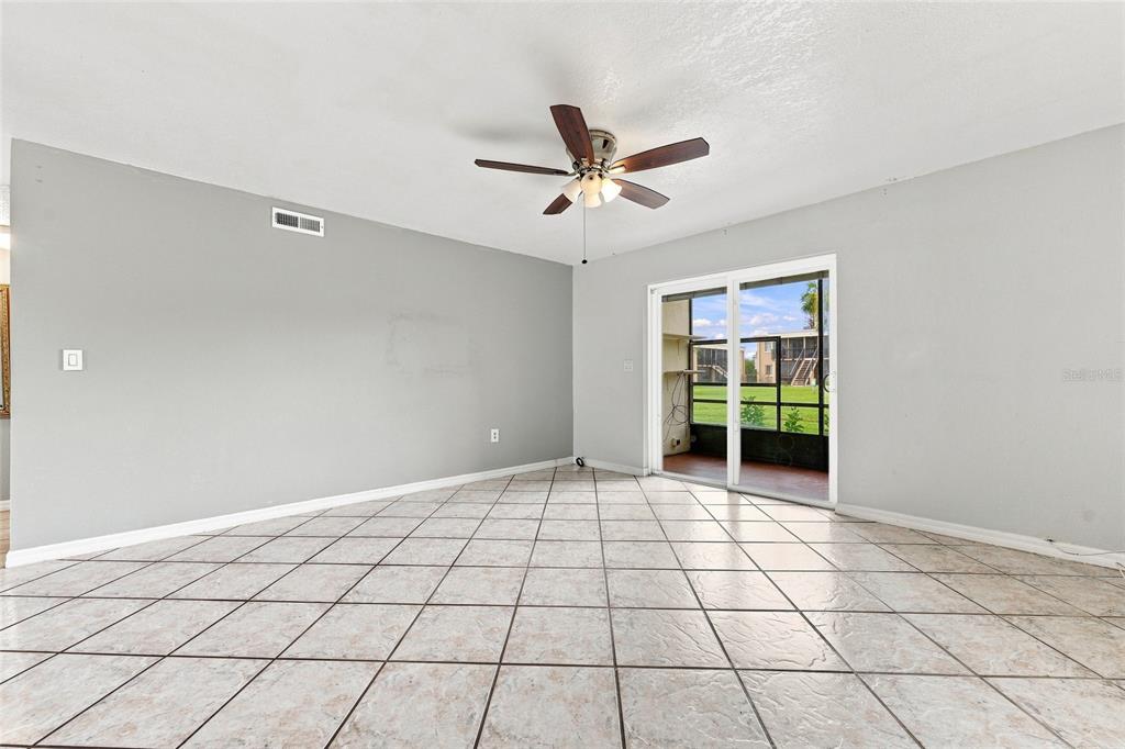 A living room features light gray walls, tiled flooring, a ceiling fan, and sliding glass doors — 1000 LAKE OF THE WOODS BOULEVARD UNIT 105E, FERN PARK, FL