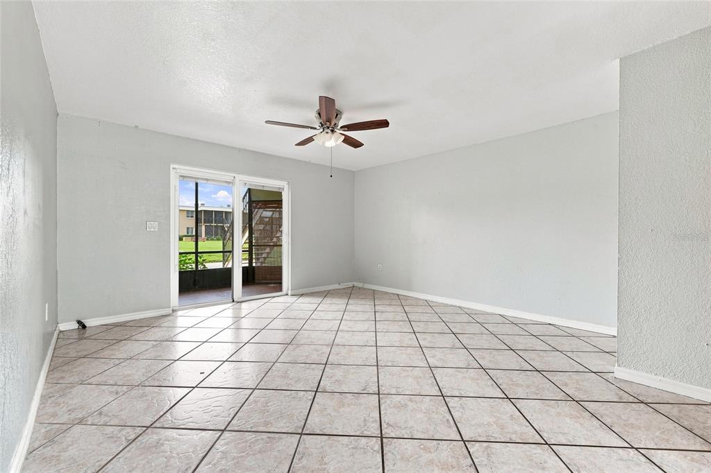 An empty room features light-colored tile flooring, a ceiling fan, and sliding glass patio doors — 1000 LAKE OF THE WOODS BOULEVARD UNIT 105E, FERN PARK, FL
