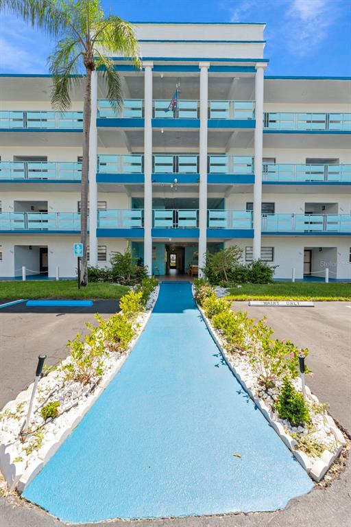 A blue walkway leads to the entrance of a multi-story apartment building with exterior balconies — 5970 80TH STREET N UNIT 309, ST PETERSBURG, FL