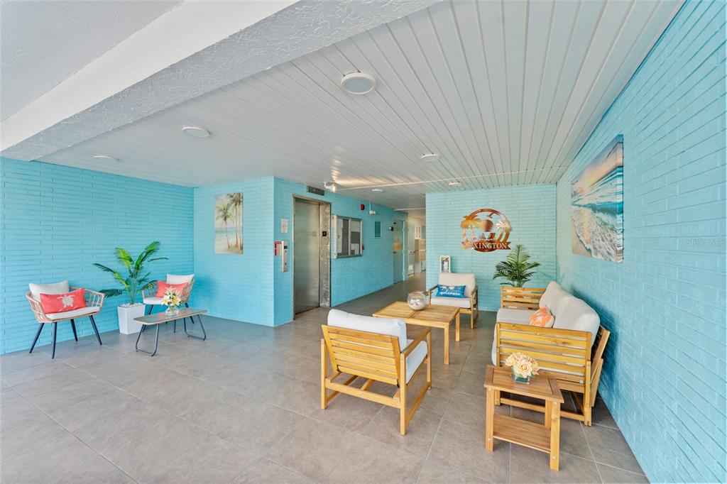 A bright blue lobby features tiled floors, an elevator, and casual wooden seating arrangements — 5970 80TH STREET N UNIT 309, ST PETERSBURG, FL