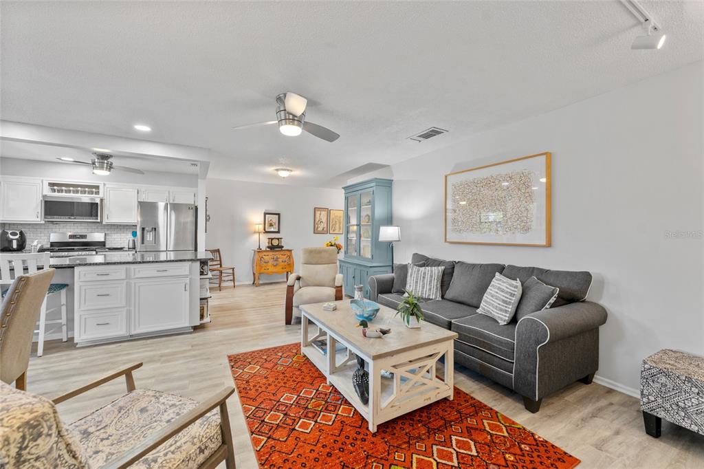 An open-concept living room features a grey sofa, a patterned orange rug, and a kitchen — 5970 80TH STREET N UNIT 309, ST PETERSBURG, FL