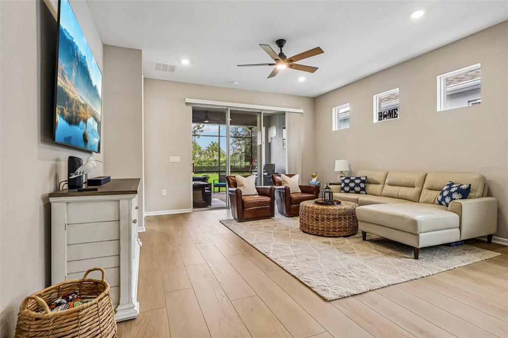 A living room features a beige sectional, two leather armchairs, a television, and sliding glass doors — 15873 GEM VIEW STREET, WINTER GARDEN, FL