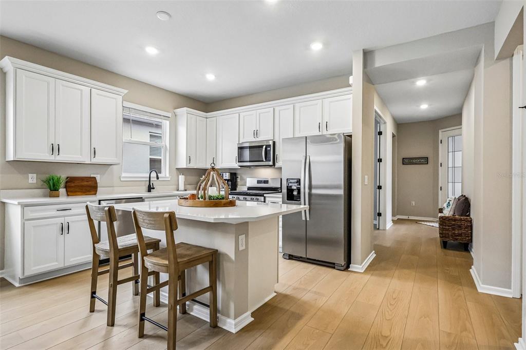 A modern kitchen features white cabinets, stainless steel appliances, a center island, and light wood flooring — 15873 GEM VIEW STREET, WINTER GARDEN, FL