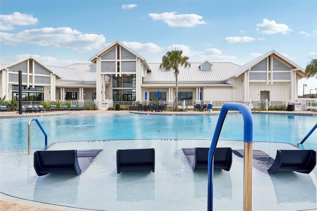 A swimming pool with in-water lounge chairs sits in front of a large clubhouse building — 15873 GEM VIEW STREET, WINTER GARDEN, FL