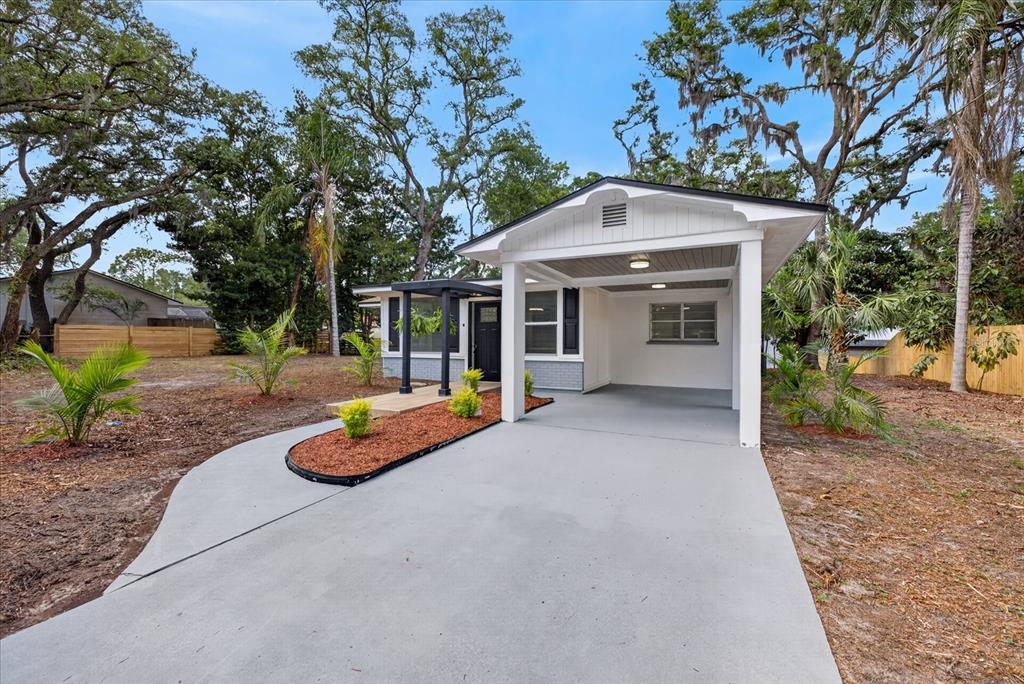 A single-story house features a concrete driveway, a covered carport, and a small landscaped garden — 7806 E 114TH AVENUE, TAMPA, FL