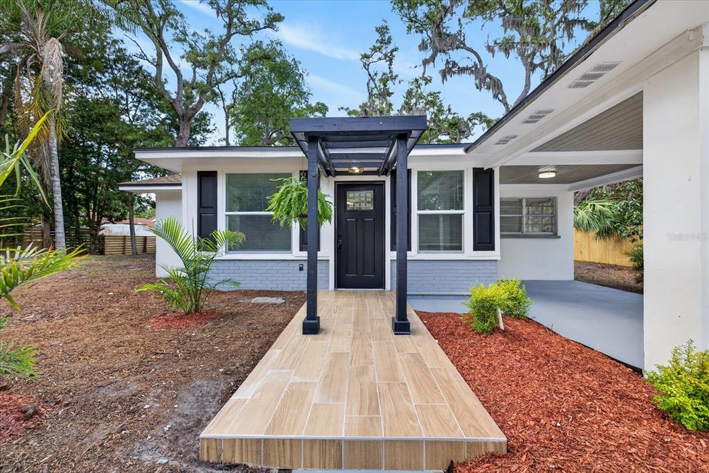 A single-story house exterior features a tiled walkway leading to a black front door — 7806 E 114TH AVENUE, TAMPA, FL