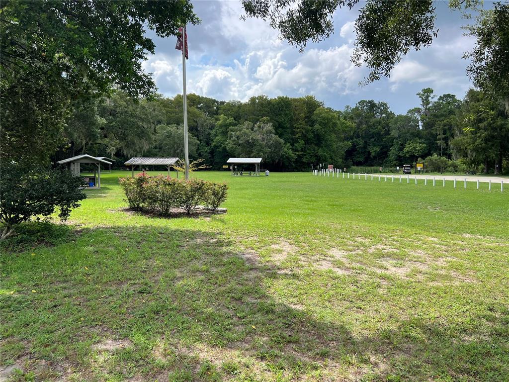 A grassy park area features several picnic pavilions, a flagpole, and a line of white posts — 18902 SW 108TH LOOP, DUNNELLON, FL