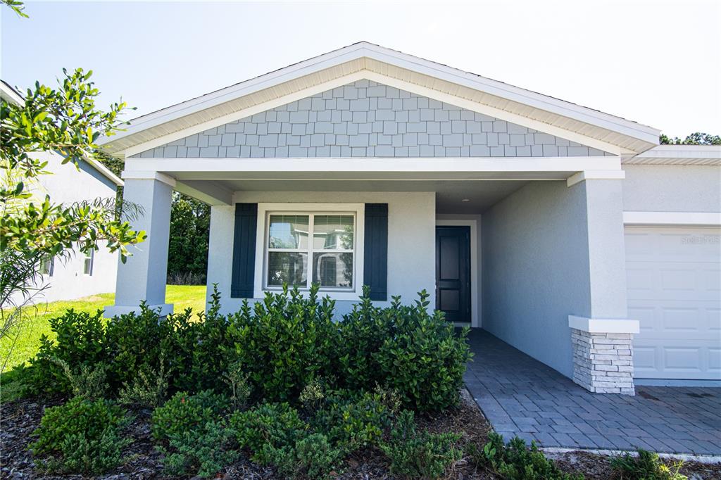 The exterior of a single-story house features a covered entryway, gray siding, and stone accents — 2946 CAMDEN WAY, DAVENPORT, FL