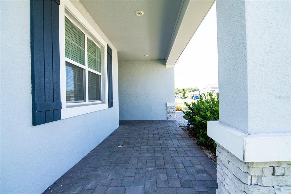 A covered porch features gray stone accents, dark paver flooring, and a window with shutters — 2946 CAMDEN WAY, DAVENPORT, FL